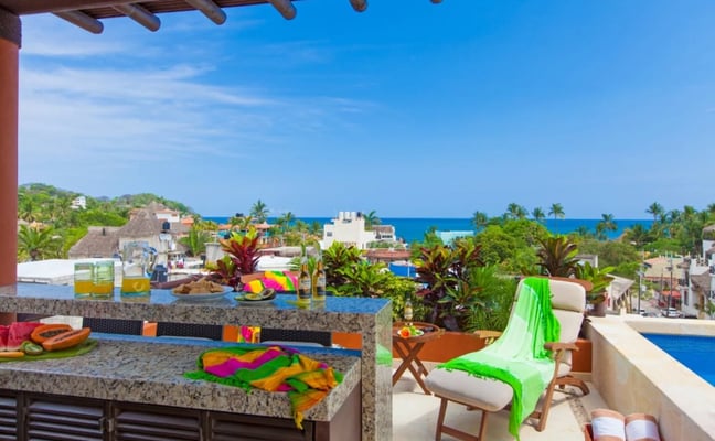 Beachfront terrace with infinity pool, colorful decorations, ocean view, and tropical vegetation